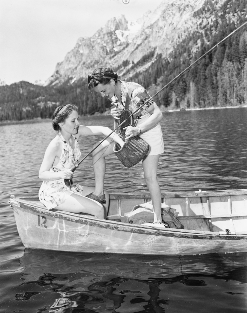 Two women stand in a canoe with fishing gear.