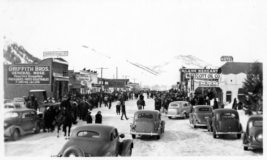 A busy street of cars, pedestrians, and horses in winter.