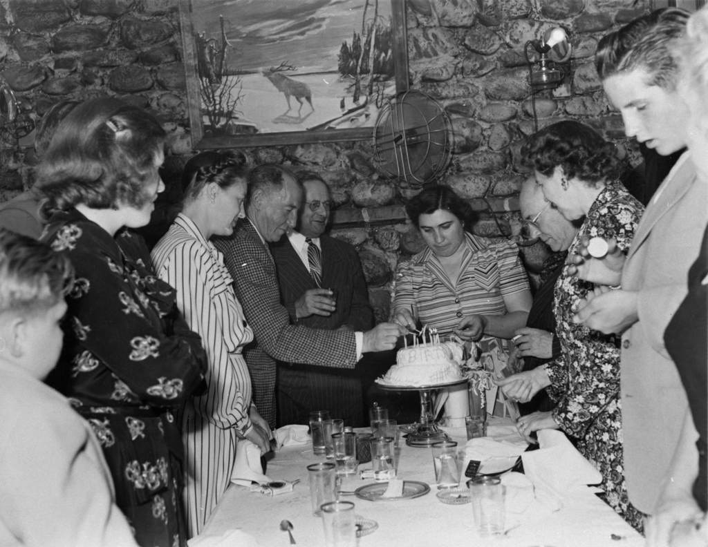 Gloria Batis lights candles on a cake in Club Rio while a crowd looks on.