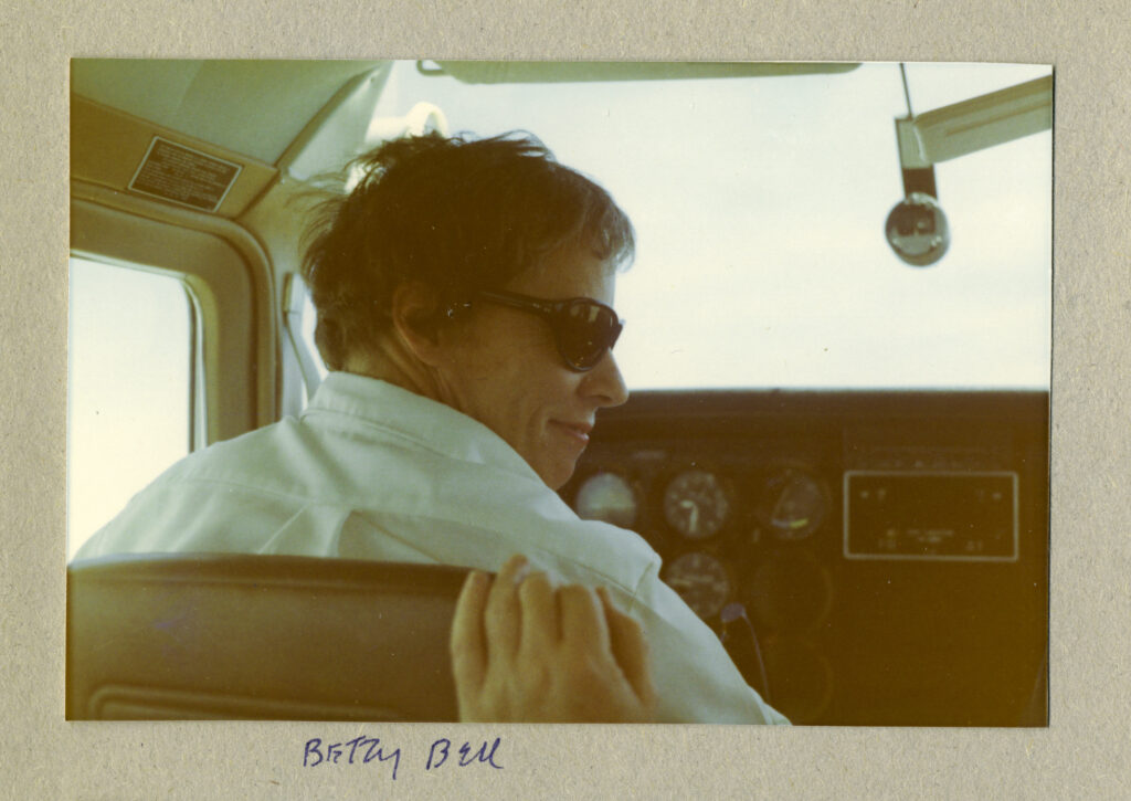 Pilot Betty Bell looks back over her shoulder sitting in the pilot seat of a small airplane.