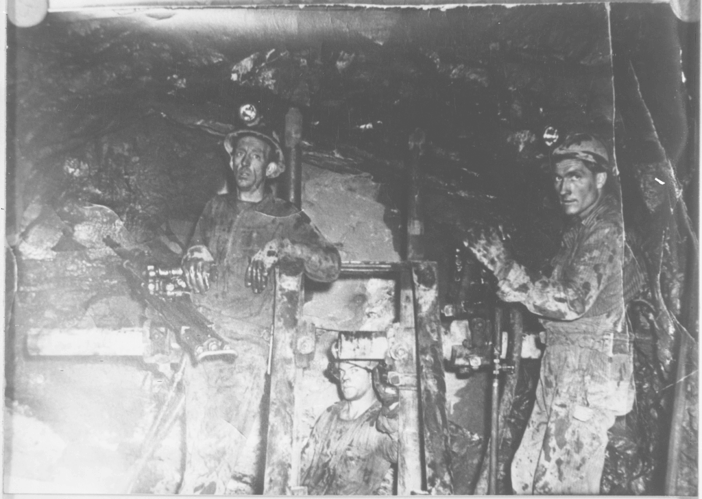 Three miners in a dark mineshaft with some machinery.