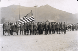 Men in World War 1 uniforms pose holding a United States flag.