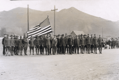 Men in World War 1 uniforms pose holding a United States flag.