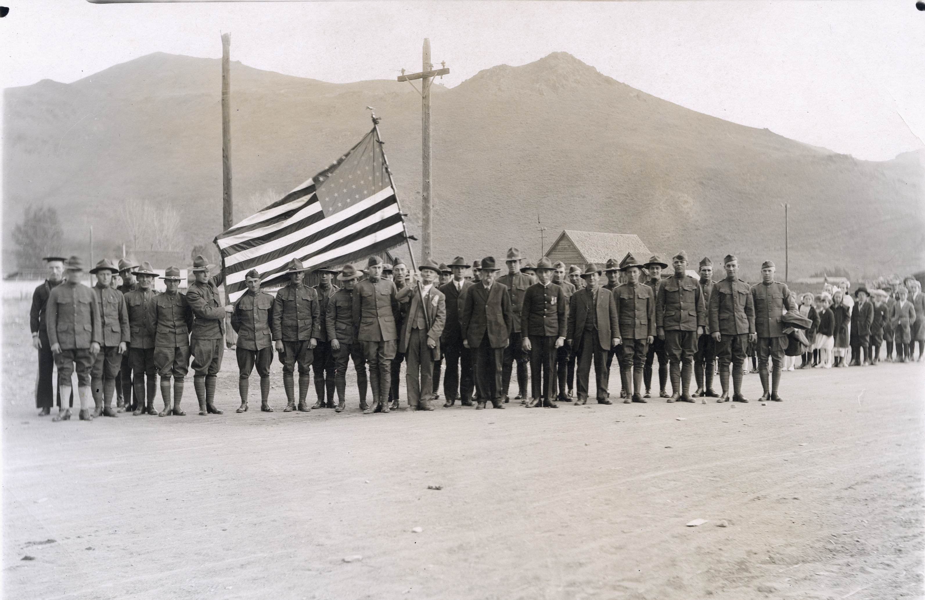 Men in World War 1 uniforms pose holding a United States flag.