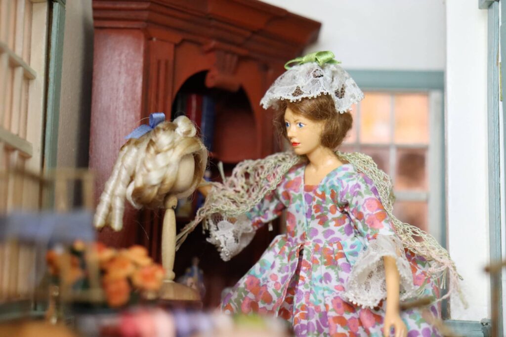 A doll tends a wig in the sewing room of the 1776 dollhouse.